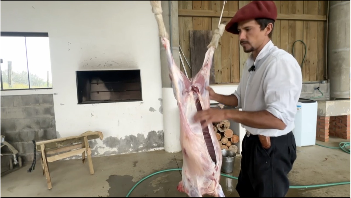Gerson carneando o cordeiro pendurado no galpão